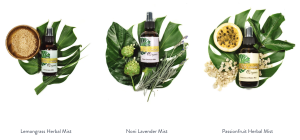 Three herbal mist bottles from Ho’omana Spa—Lemongrass, Noni Lavender, and Passionfruit—displayed with Hawaiian botanicals like salt, noni, lavender, and passionfruit on green ti leaves.